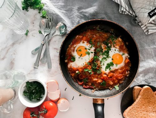 tomato soup on black cooking pan beside stainless steel fork and bread knife
