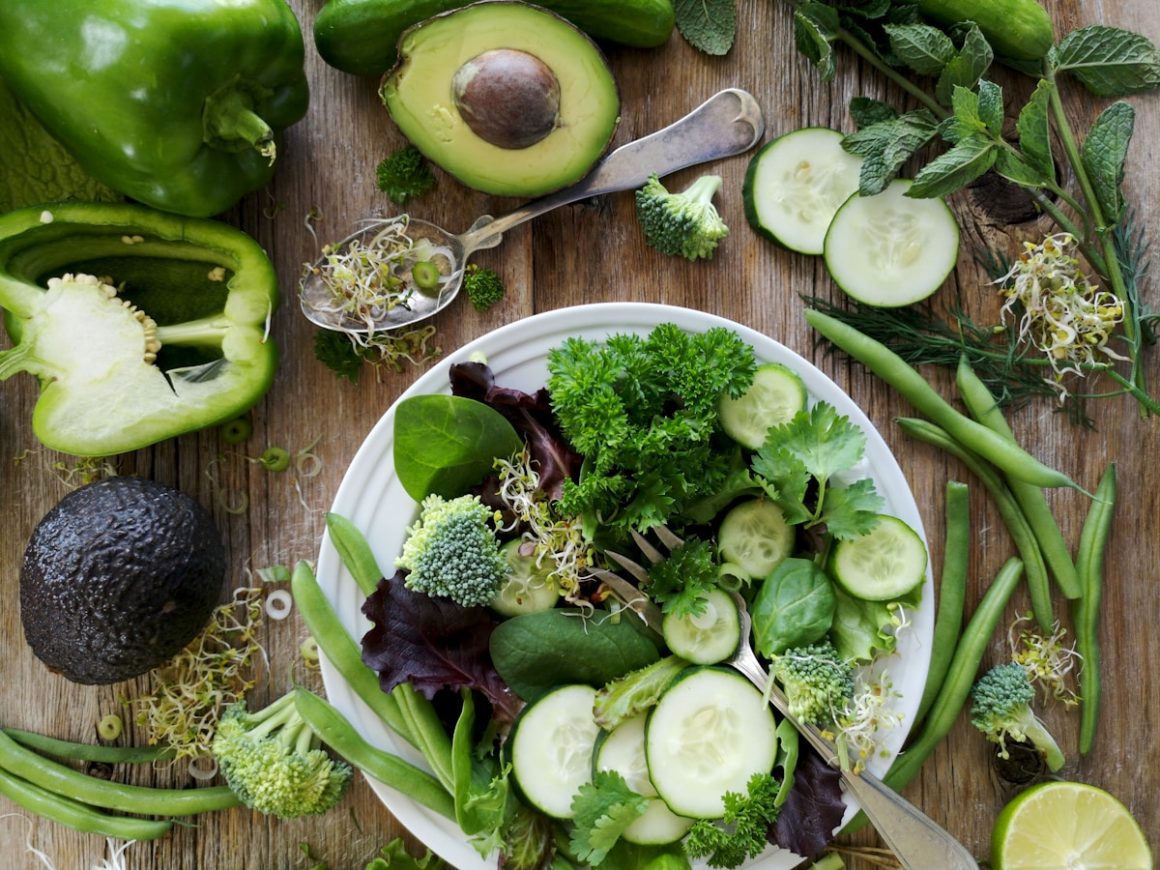sliced broccoli and cucumber on plate with gray stainless steel fork near green bell pepper, snowpea, and avocado fruit