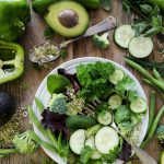 sliced broccoli and cucumber on plate with gray stainless steel fork near green bell pepper, snowpea, and avocado fruit